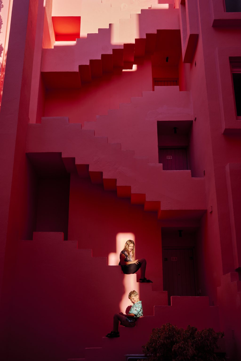Two of the kids sitting in patches of sunlight on the red staircases of Muralla Roja