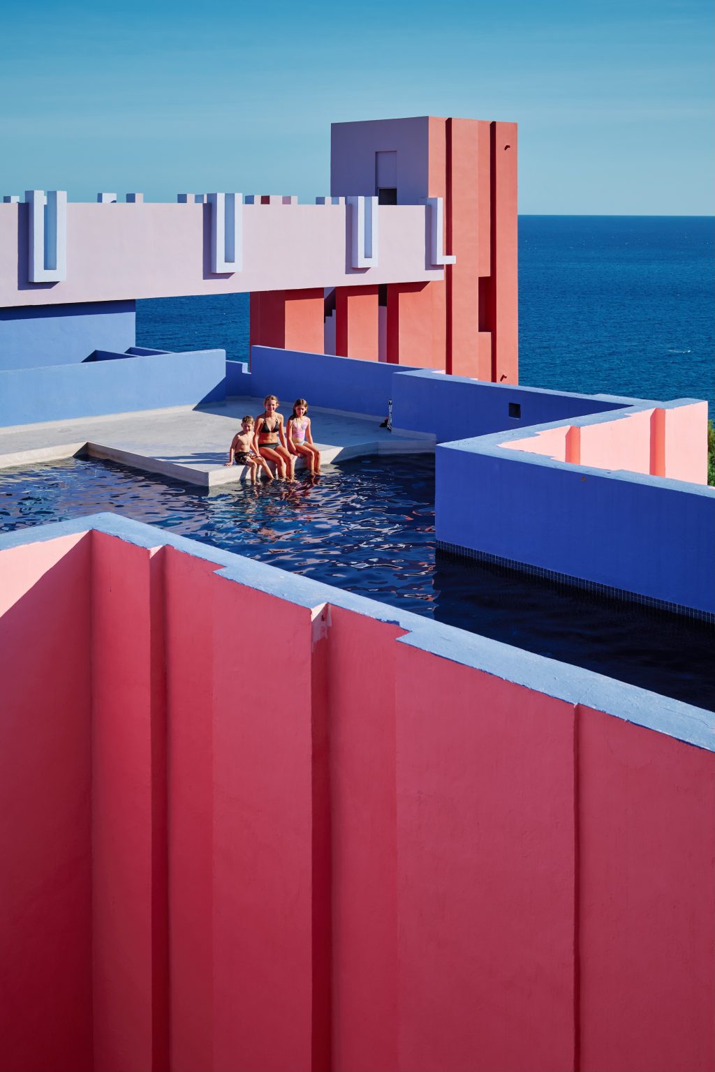 Three kids at the rooftop pool of Muralla Roja with the Mediterranean behind