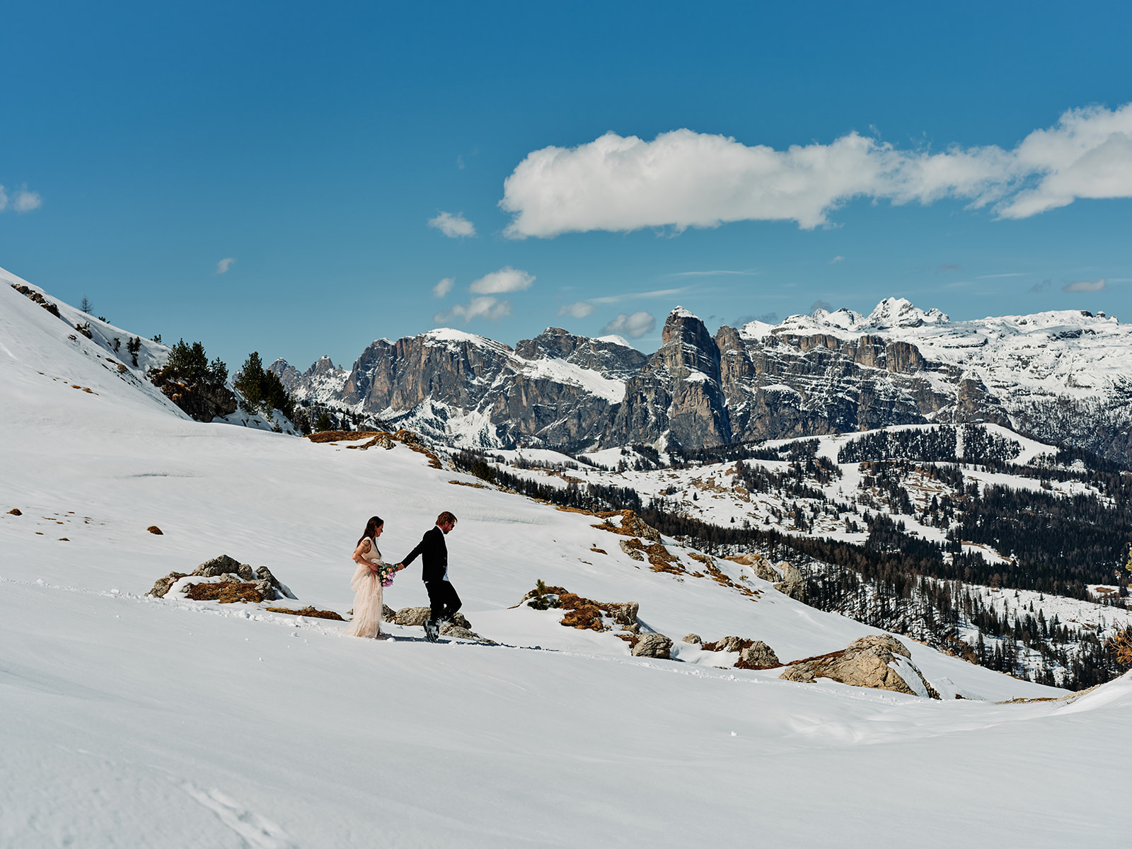 Elopement couple small in a vast snowy Dolomites valley at Passo Gardena, Val Gardena - Nordica Photography
