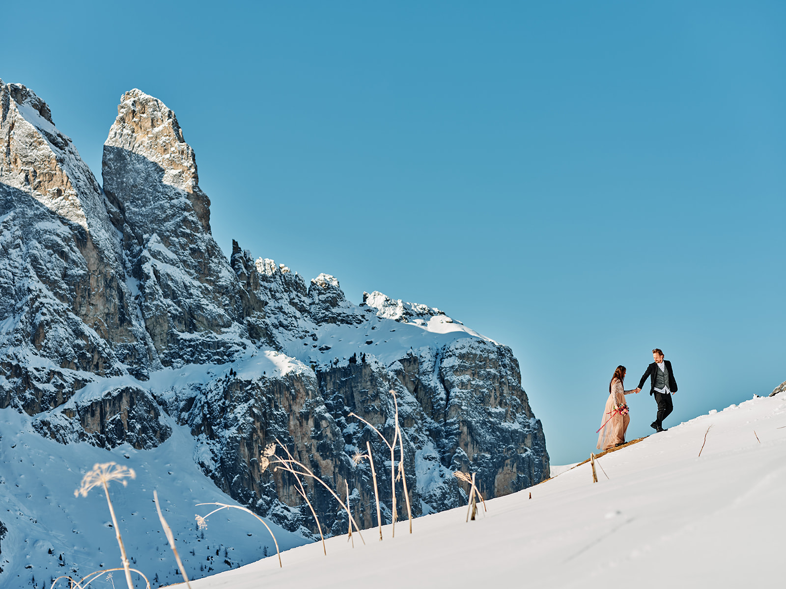 Bride and groom beneath a snow-covered Dolomite peak at Passo Gardena, Val Gardena - Nordica Photography