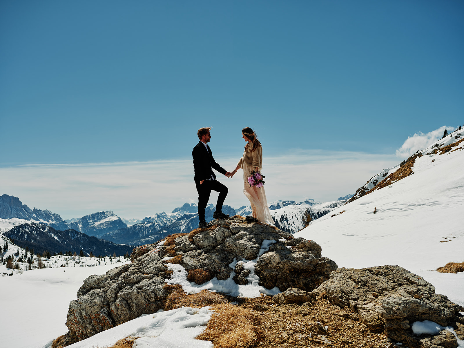 Winter wedding couple on a rock outcrop above the snow at Passo Gardena, Dolomites - Nordica Photography