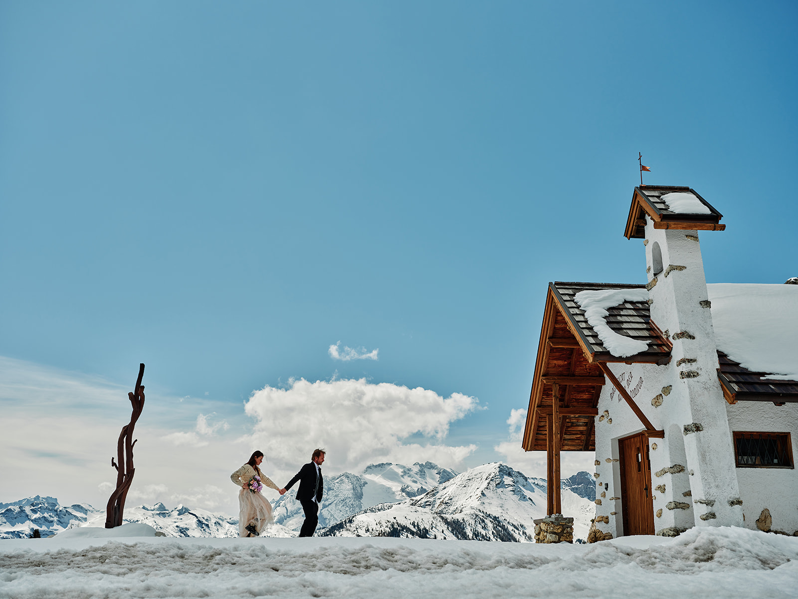 Couple by the little alpine chapel in the snow at Passo Gardena, Val Gardena Dolomites - Nordica Photography