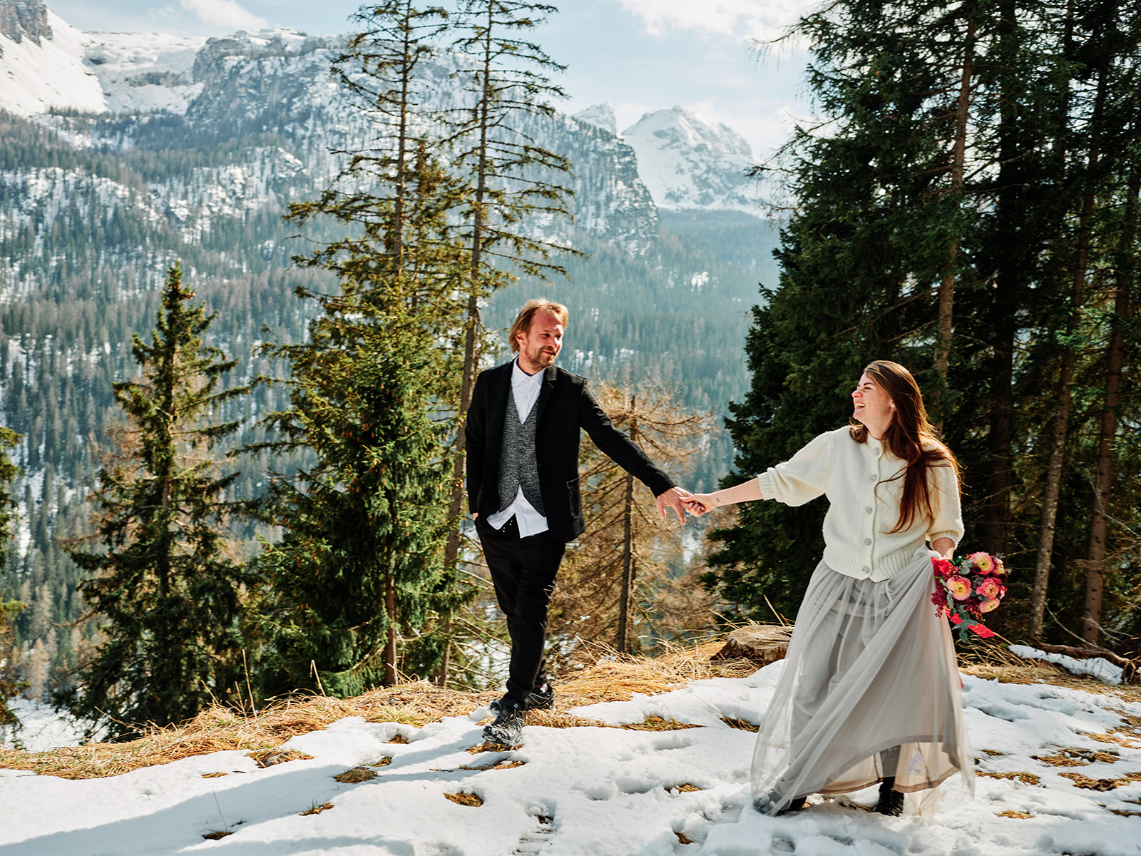 Bride and groom walking hand in hand through the snow at Passo Gardena, Dolomites - Nordica Photography