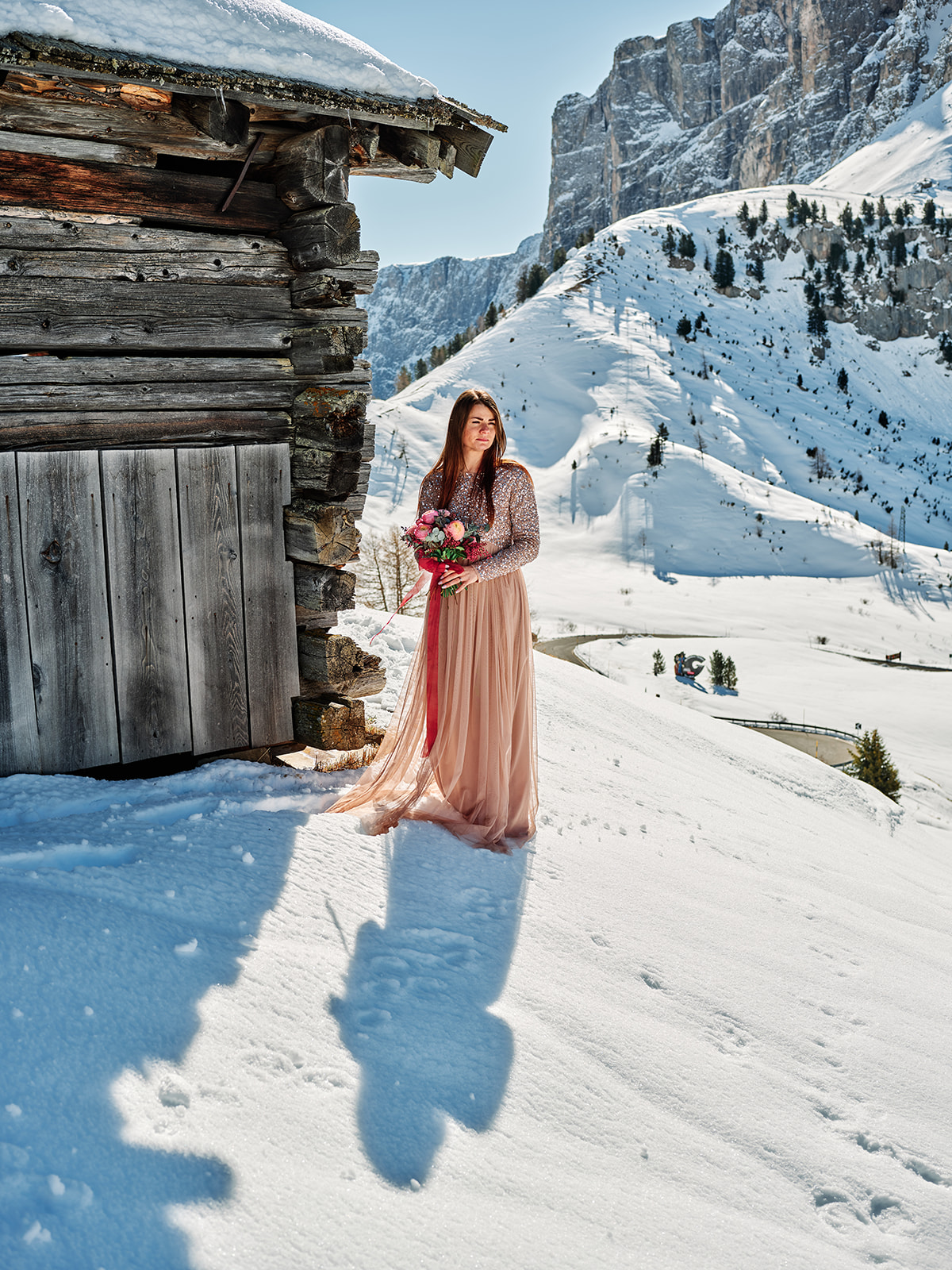 Bride in the snow by a weathered wooden hut at Passo Gardena, a Dolomites winter wedding - Nordica Photography
