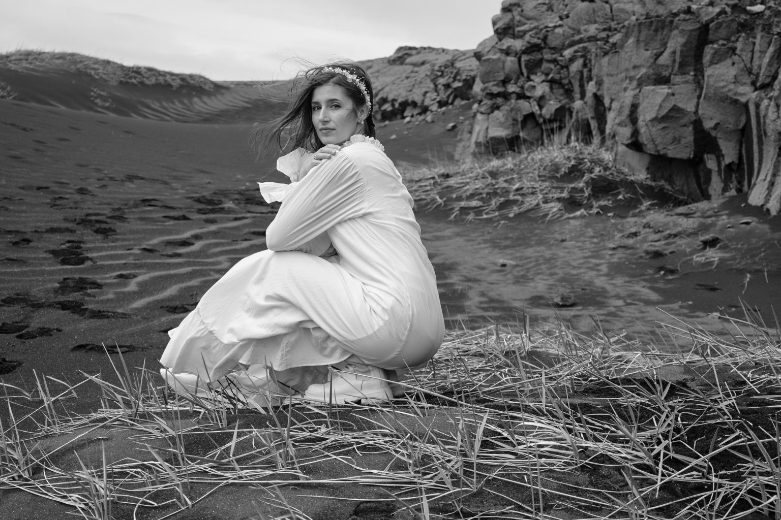 Bride crouching by dark lava rock on the Reykjanes peninsula, black and white