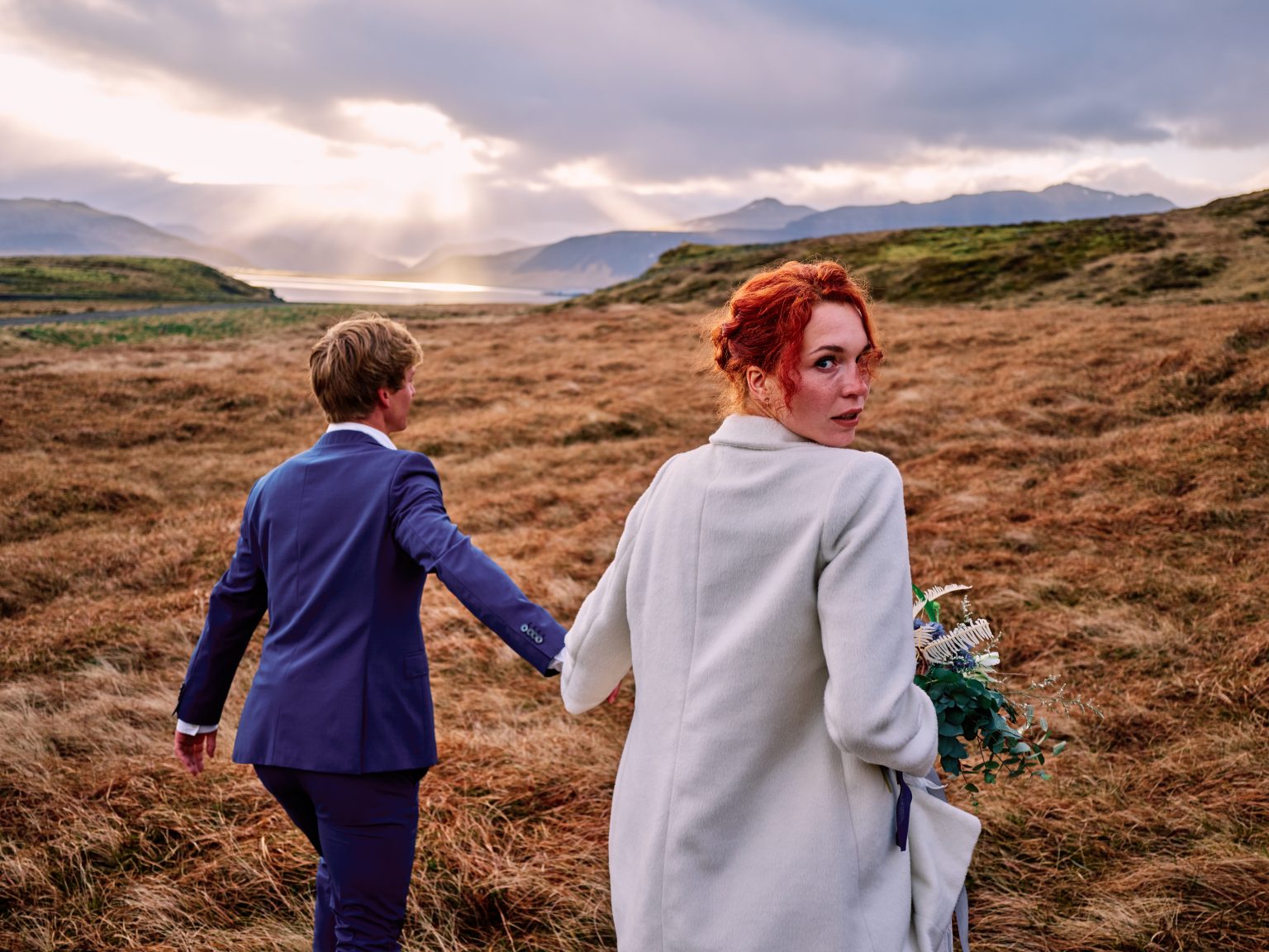 Couple walking through golden grass below Kirkjufell