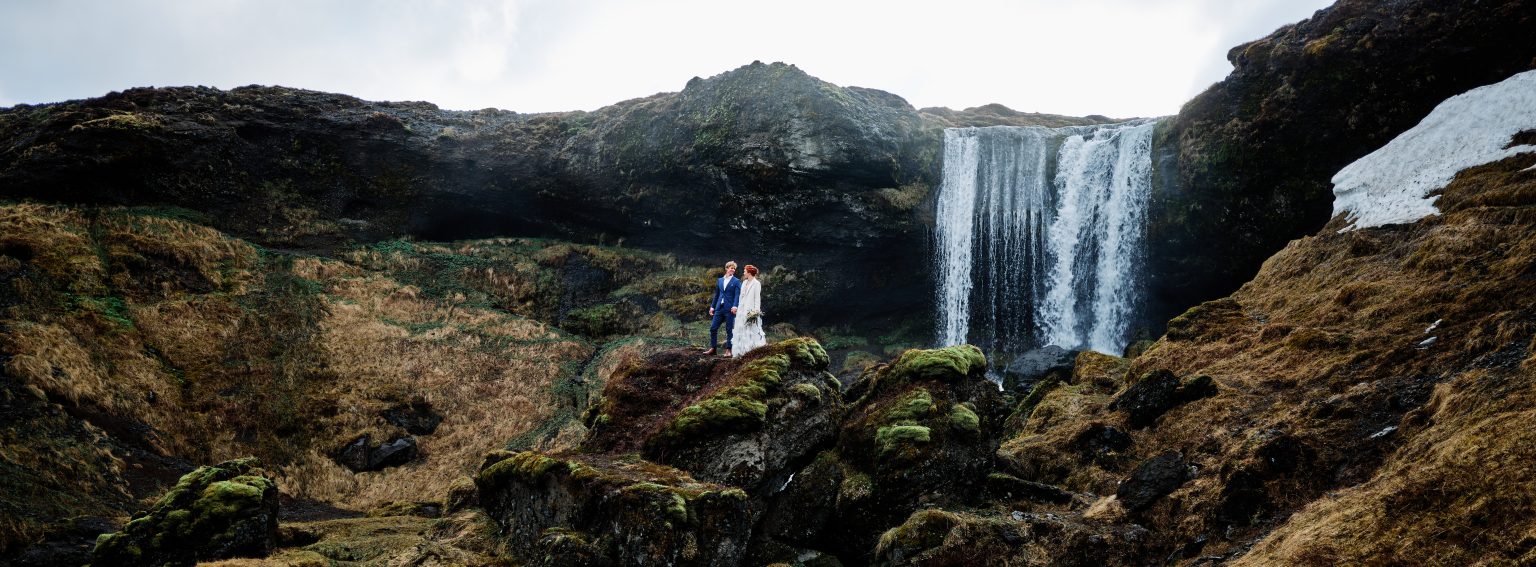 The couple small in front of a large Icelandic waterfall