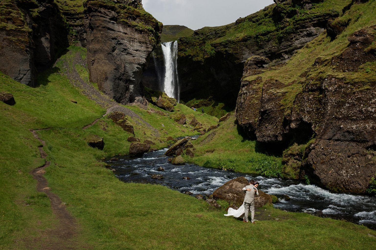 Bride and groom small in the Kvernufoss canyon after their vows, South Iceland elopement