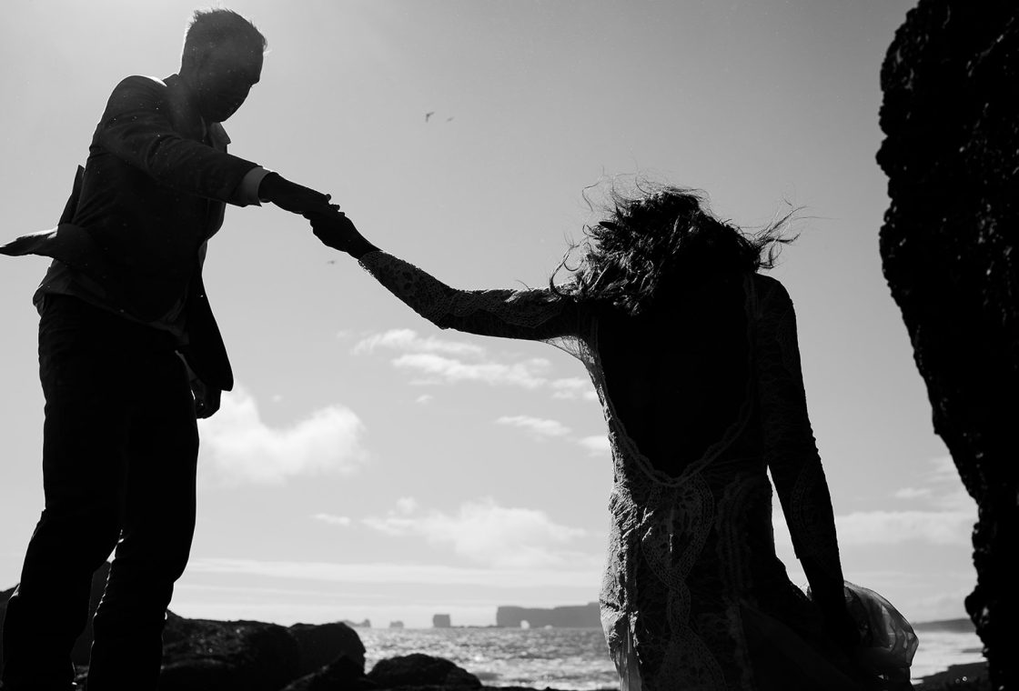 Bride and groom reaching for one another in silhouette at the Reynisdrangar sea stacks, South Iceland elopement