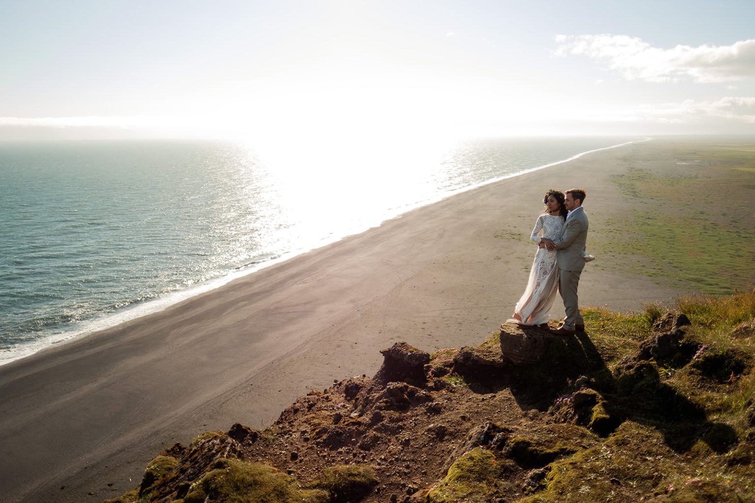 Couple small against a vast black headland at Dyrholaey, South Iceland elopement