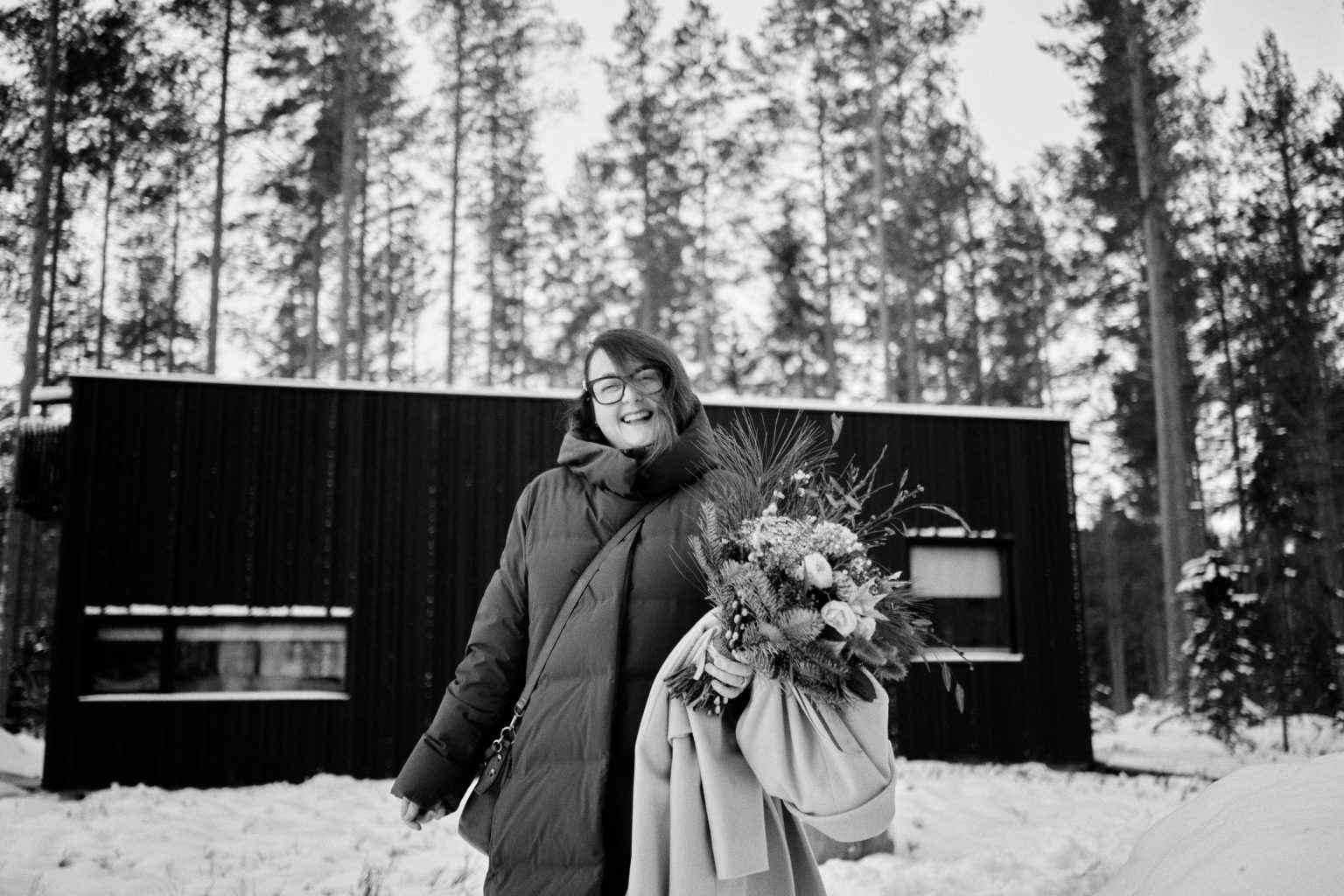 Sam and Rob by the black cabin at Hop Farm Beach, a winter elopement in Sweden