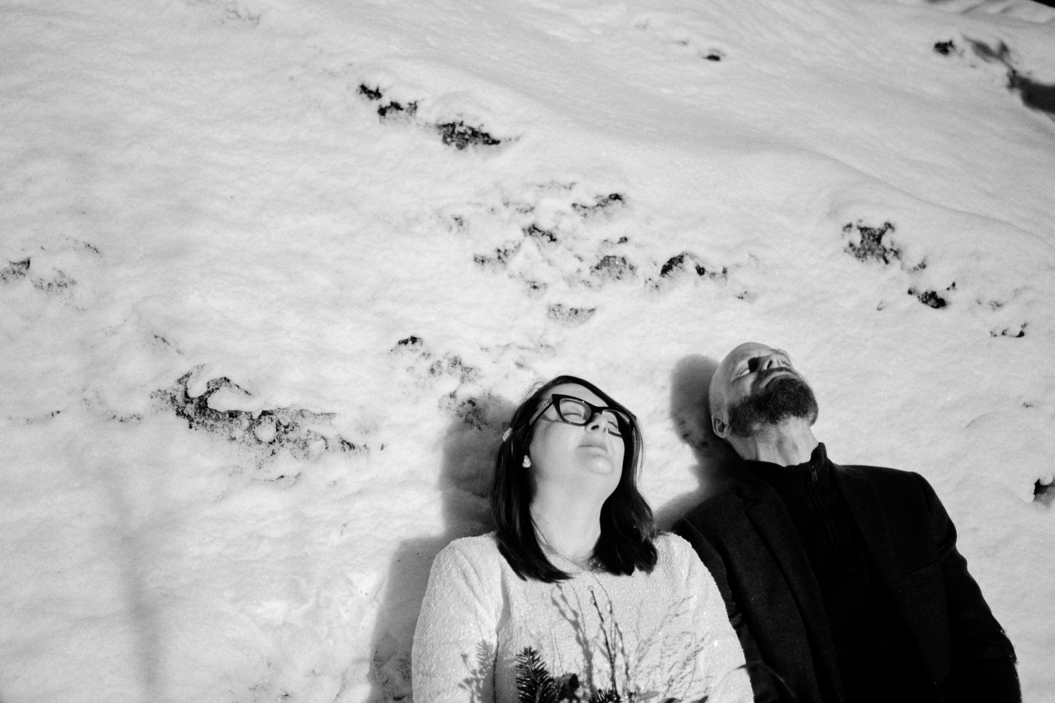 Black and white, Sam and Rob lying in the snow, a Nordic elopement