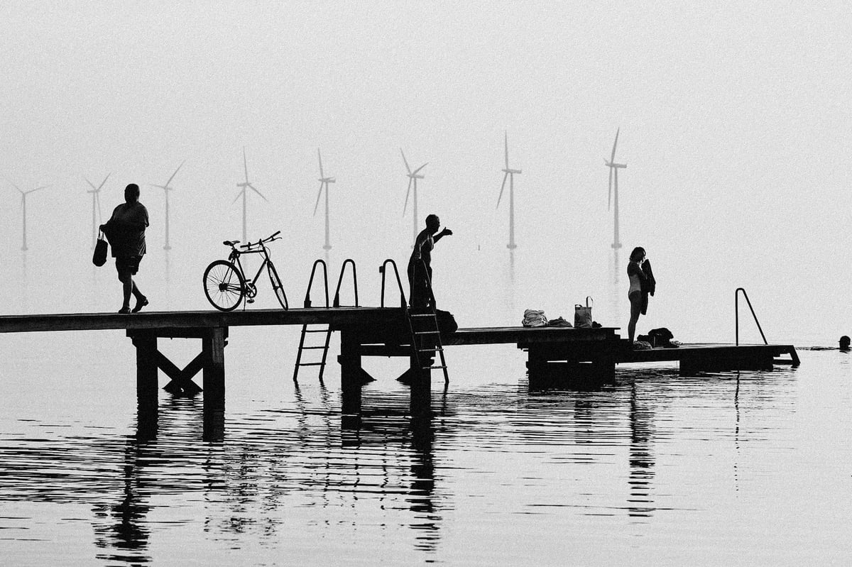 A jetty and wind turbines on flat water, black and white