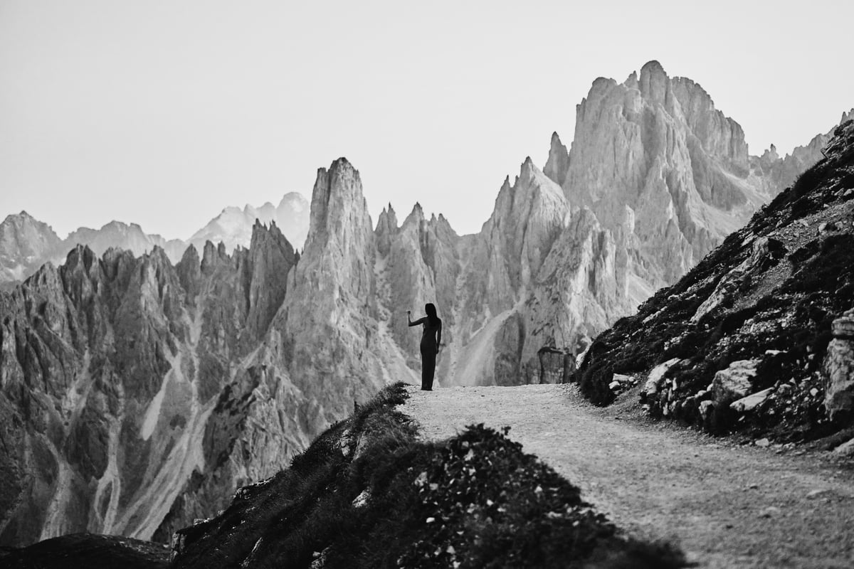 A walker on a path below jagged peaks in the Dolomites, black and white