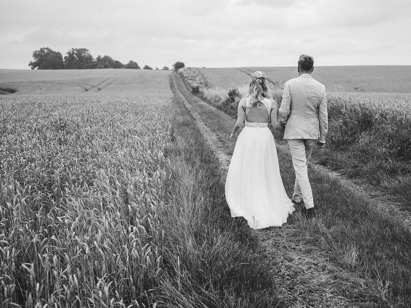 Bride and groom walking a tramline through the wheat, black and white