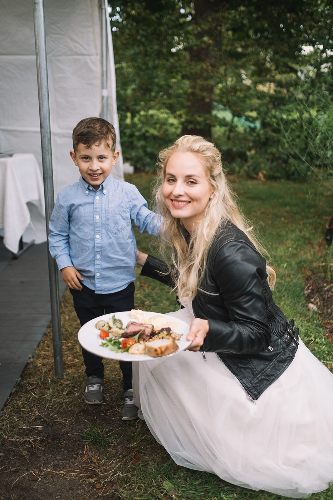 The bride carrying plates across the grass with a young guest