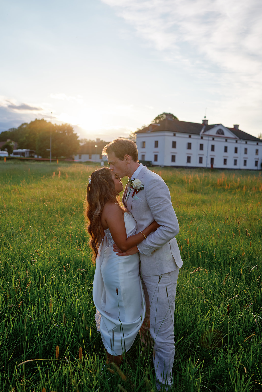 The couple in the tall grass with the manor behind them at golden hour
