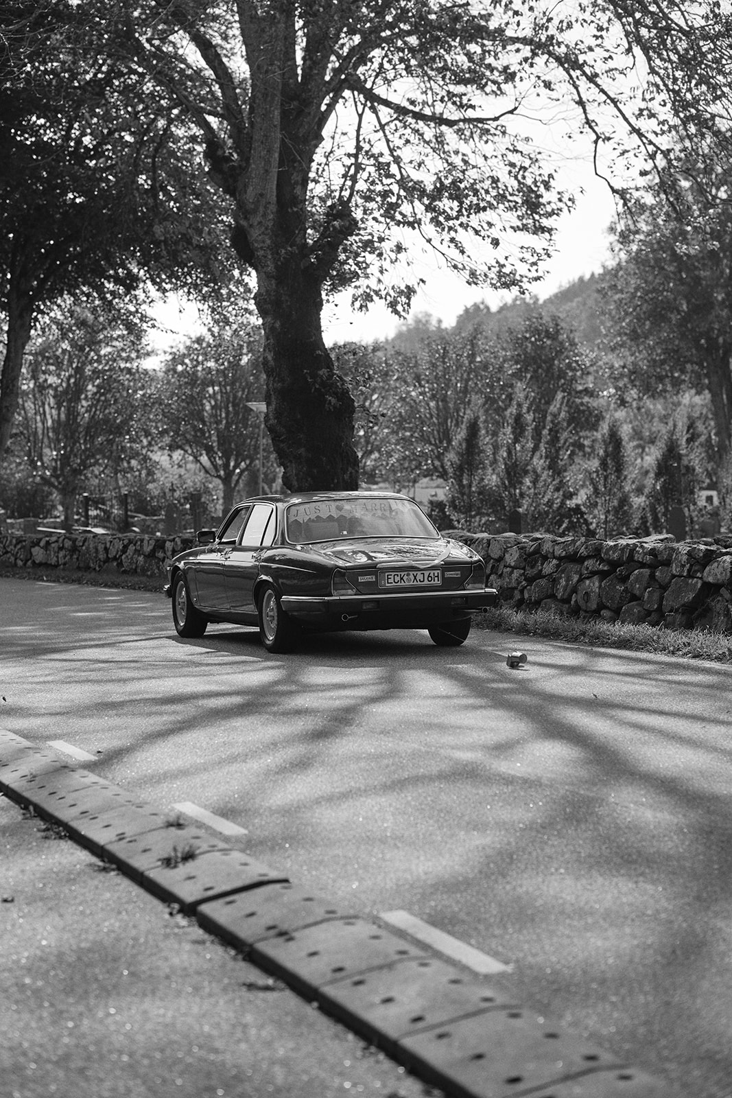 The wedding car driving away down a tree lined lane