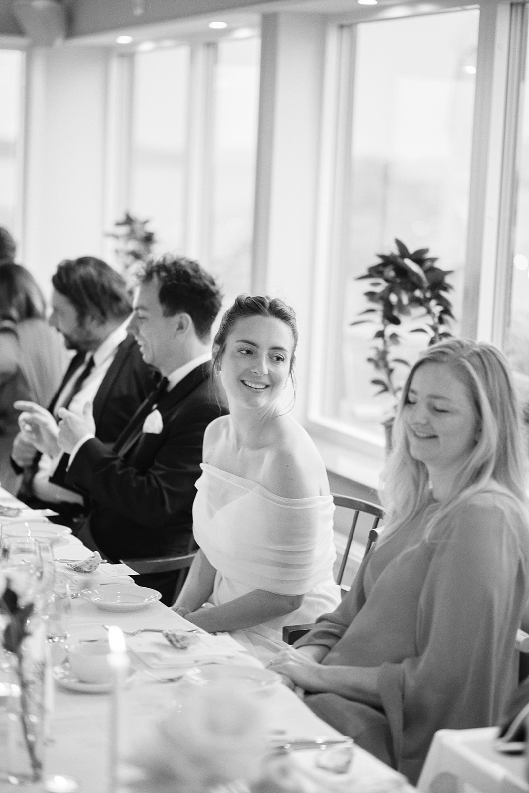 The bride laughing with a guest at the dinner table, black and white