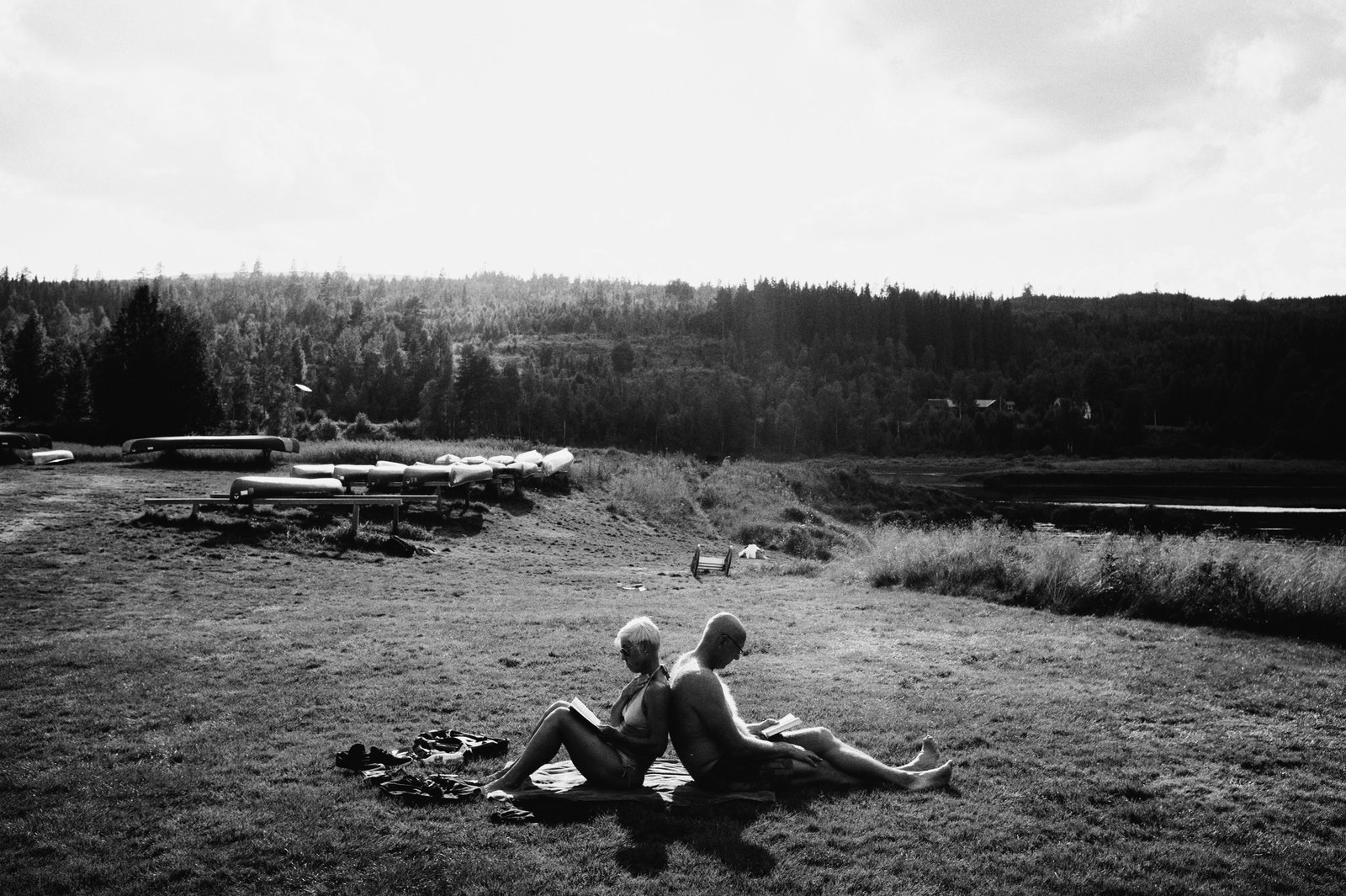 Two people sitting on a shore by the boats, black and white