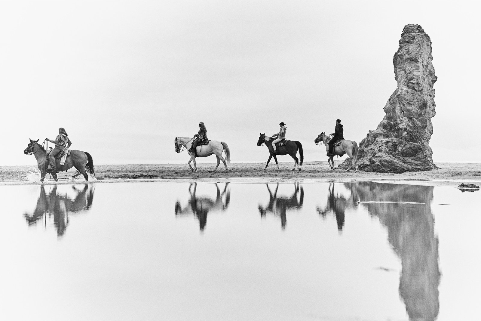 Riders reflected on a wet beach, black and white
