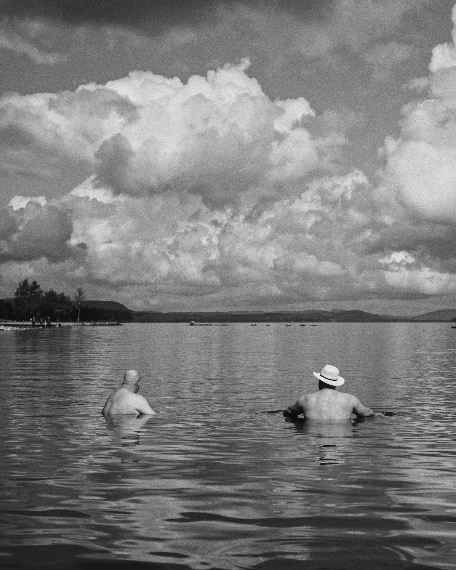 Two bathers in a lake beneath a large cloud, black and white