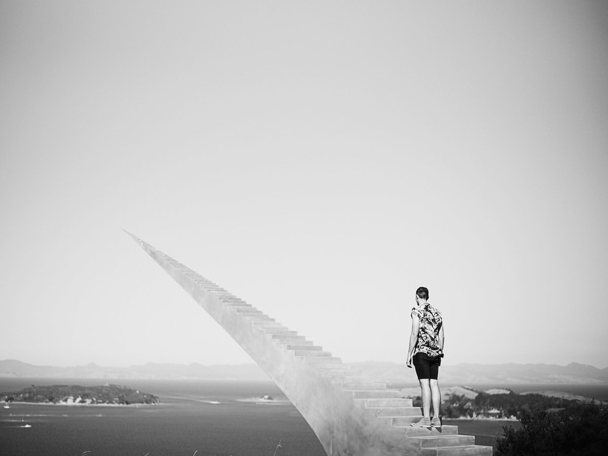 A figure on a concrete structure above the water, black and white