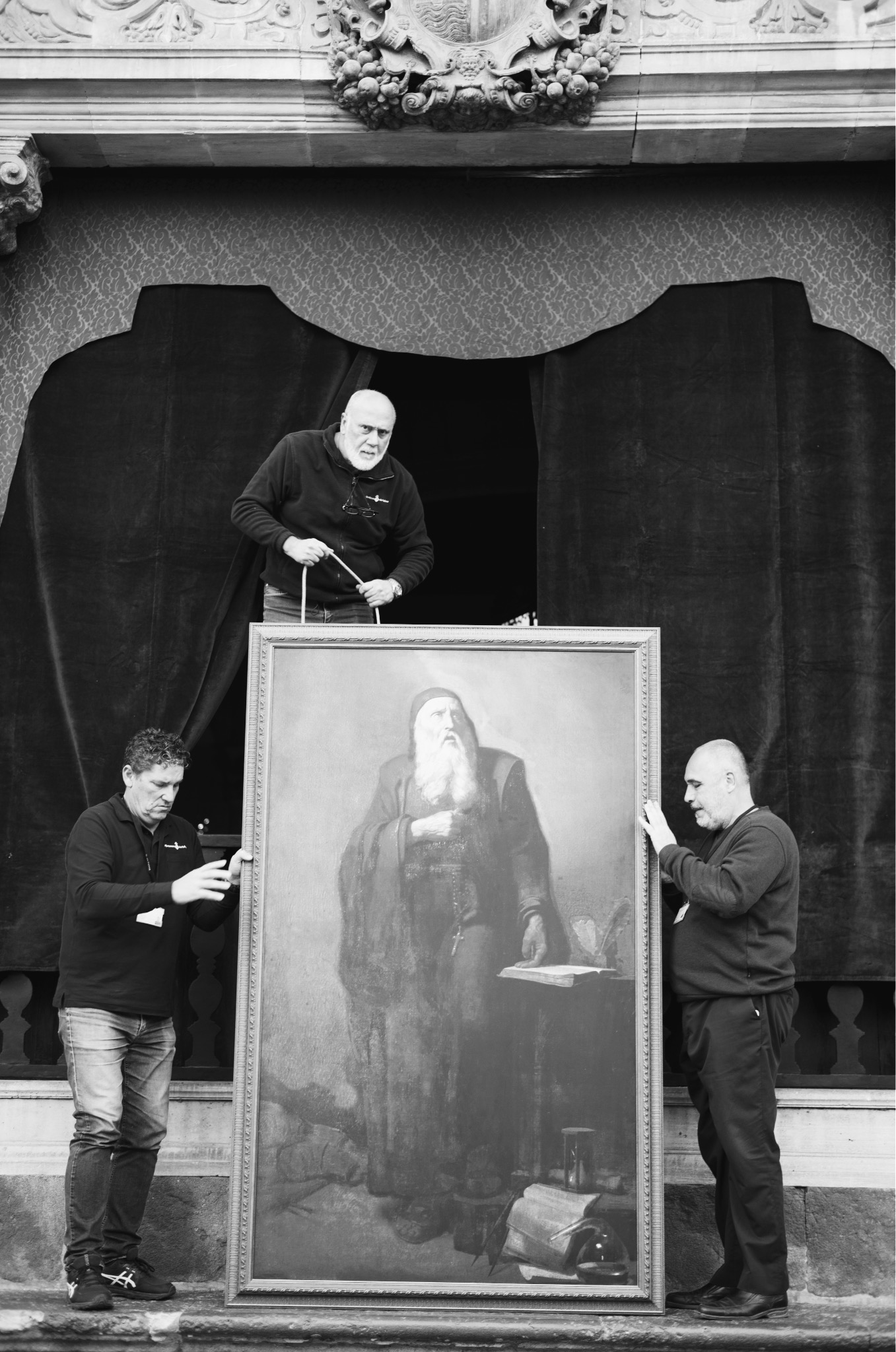Three men moving a large painting in a gilded room, black and white